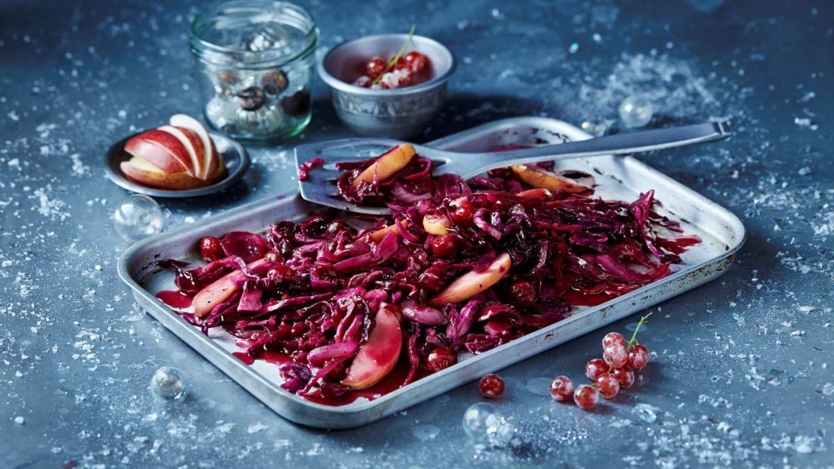 Ein Blech mit Apfel-Rotkohl auf vereistem Untergrund, daneben liegen gefrostete Johannisbeeren und einige weitere Zutaten.