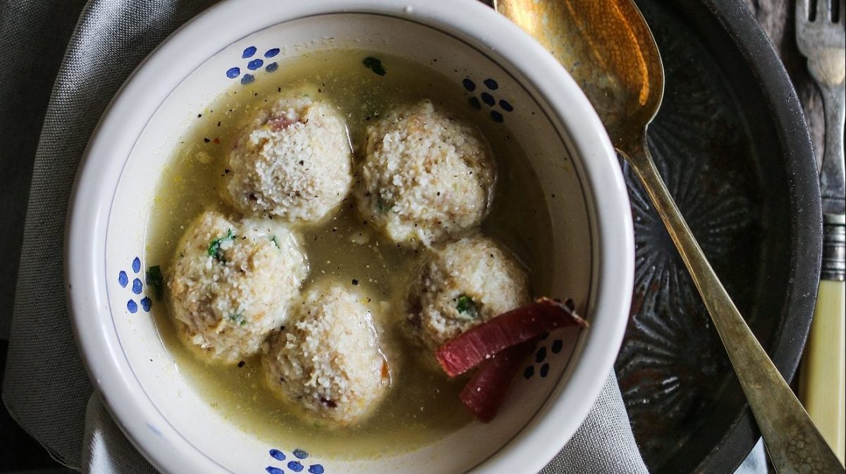 Unsere bayrischen Semmelknödel mit Speck schwimmen in einer Gemüsebrühe in einer Schale.