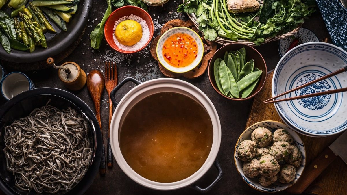 Vogelpespektive: Mehrere Schüsseln und Schalen, die mit unterschiedlichen Flüssigkeiten und Lebensmitteln befüllt sind. Es handelt sich um ein chinesisches Fondue