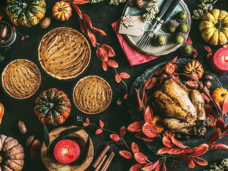 Ein Thanksgiving-Dinnertisch in der Draufsicht, darauf ein Truthahn, Kuchen, Aufläufe und herbstliche Deko.