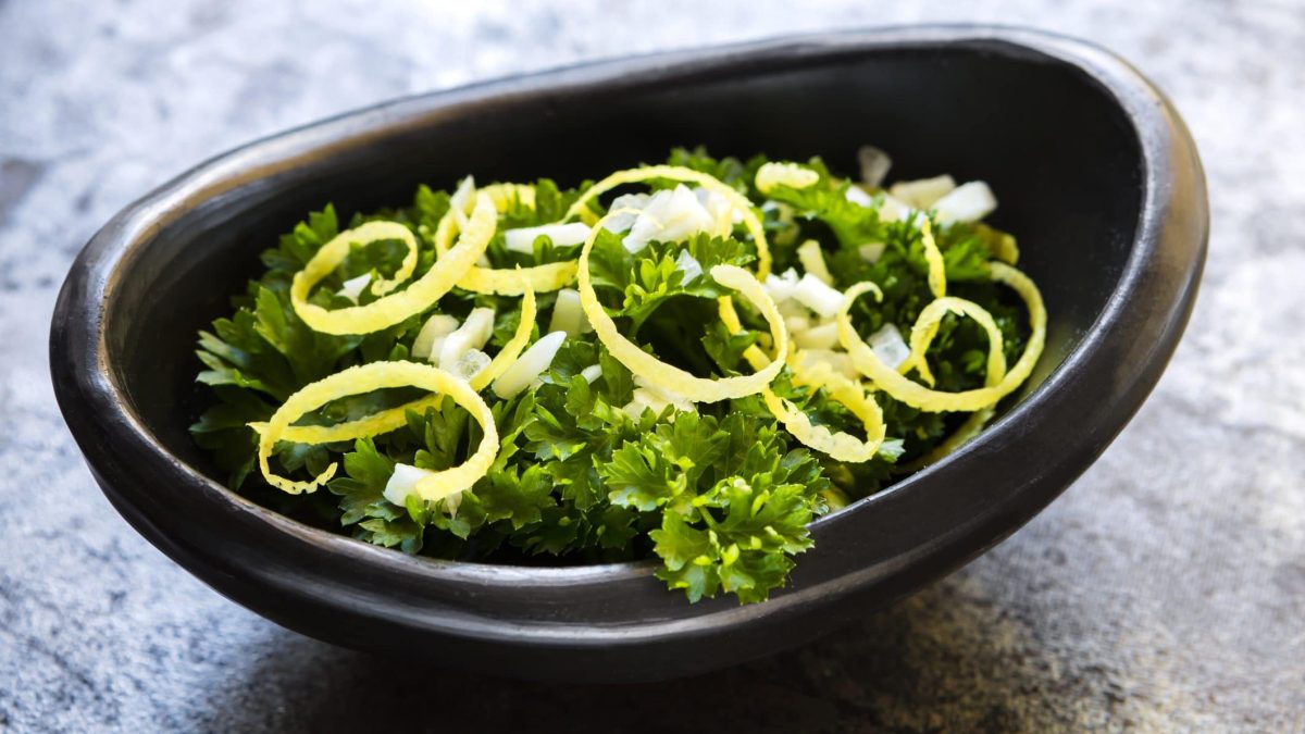 In einer ovaeln schwarzen Schale sind Petersilienblätter und Zitronenzesten als Gremolata.