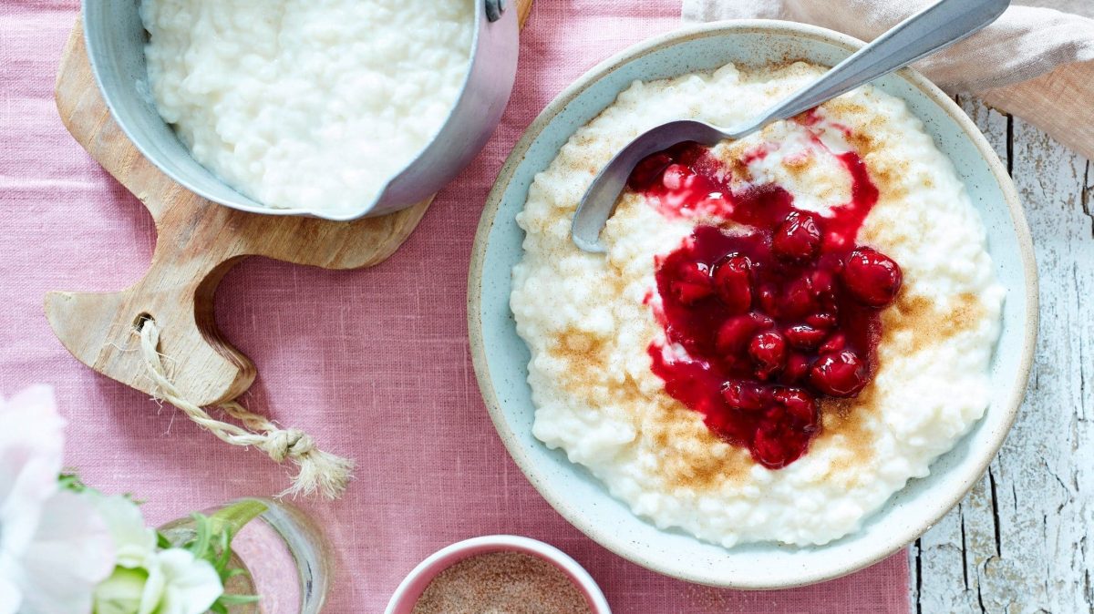 Unser Milchreis mit Kirschen angerichtet in einer Dessertschüssel auf einer rosa Tischdecke.