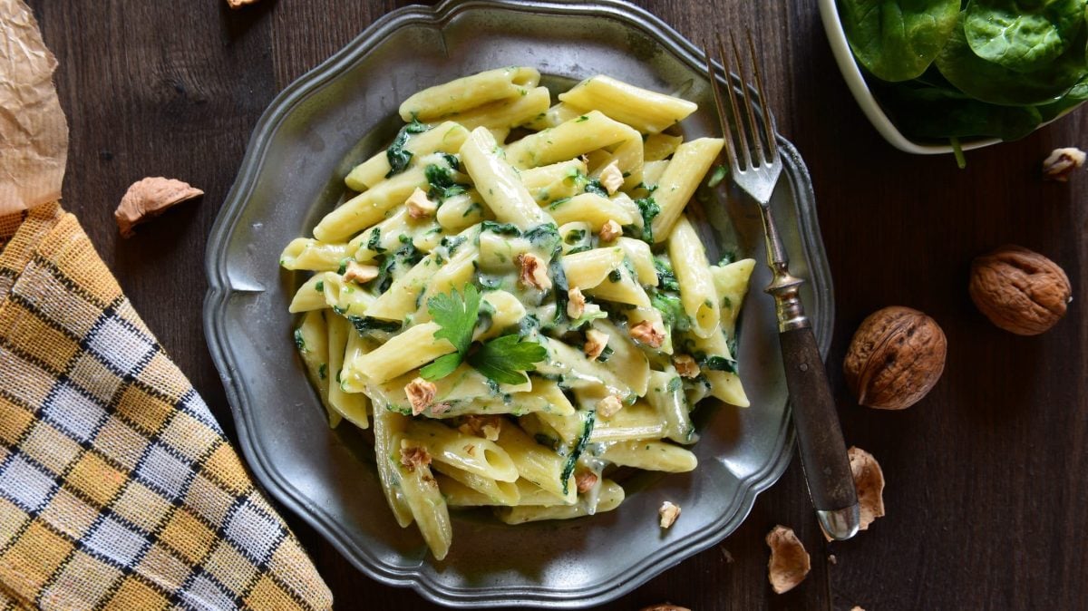 Draufsicht: Auf einem Teller liegen Penne, eine italienische Nudelsorte. Die Penne sind mit Gorgonzola, Spinat und Walnüssen zubereitet.