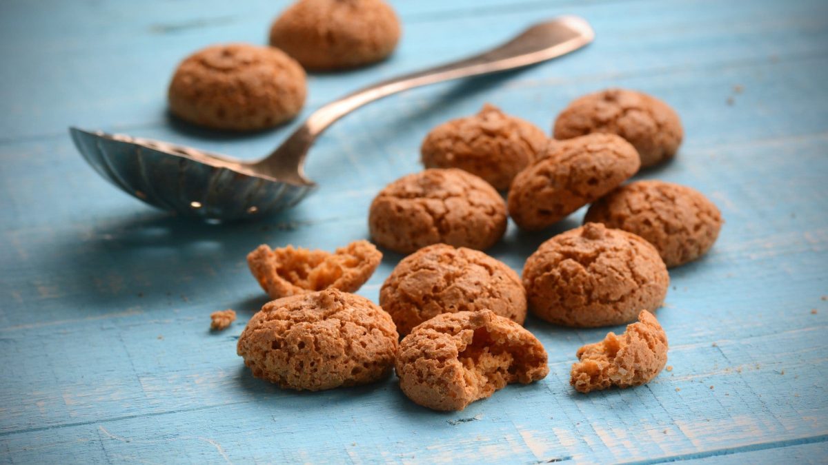 Auf blauem Holz liegen selbst gemachte Amaretti-Kekse und ein Löffel.