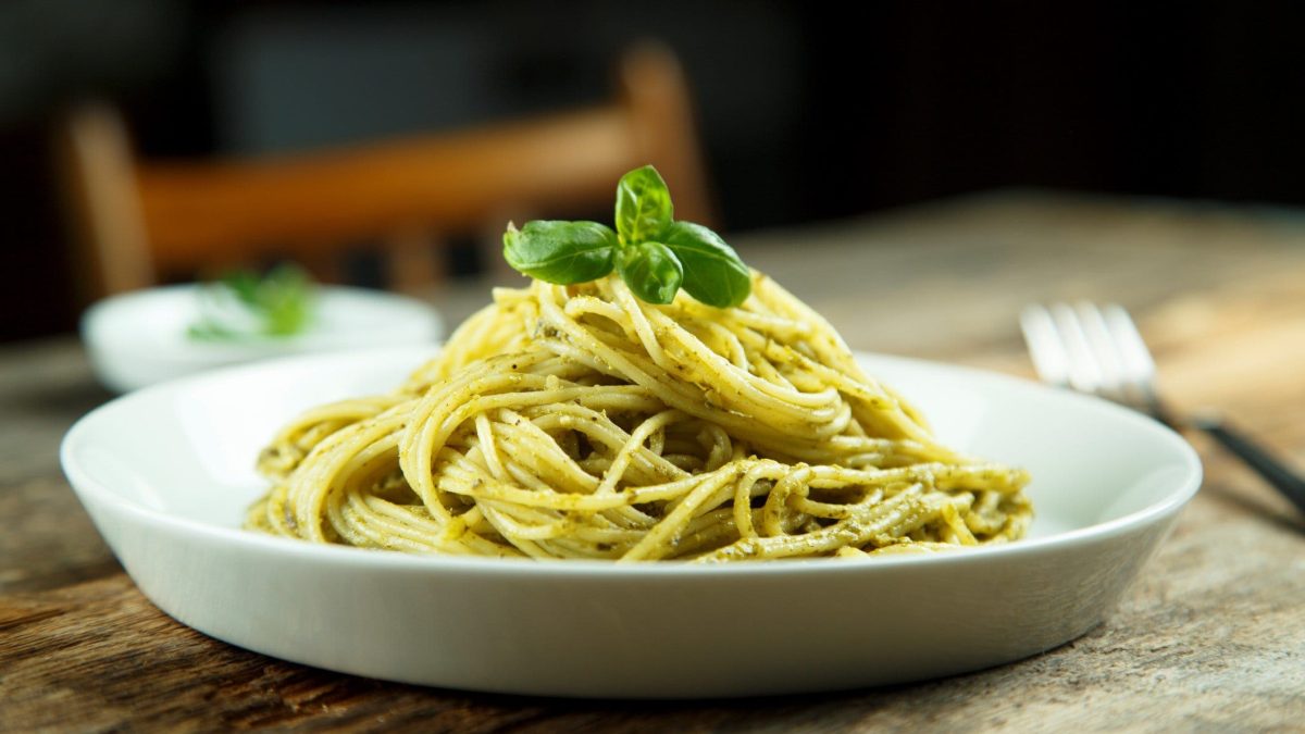 Ein Teller Spaghetti mit Gin-Soße, dekoriert mit Basilikum, steht auf einem Holztisch.