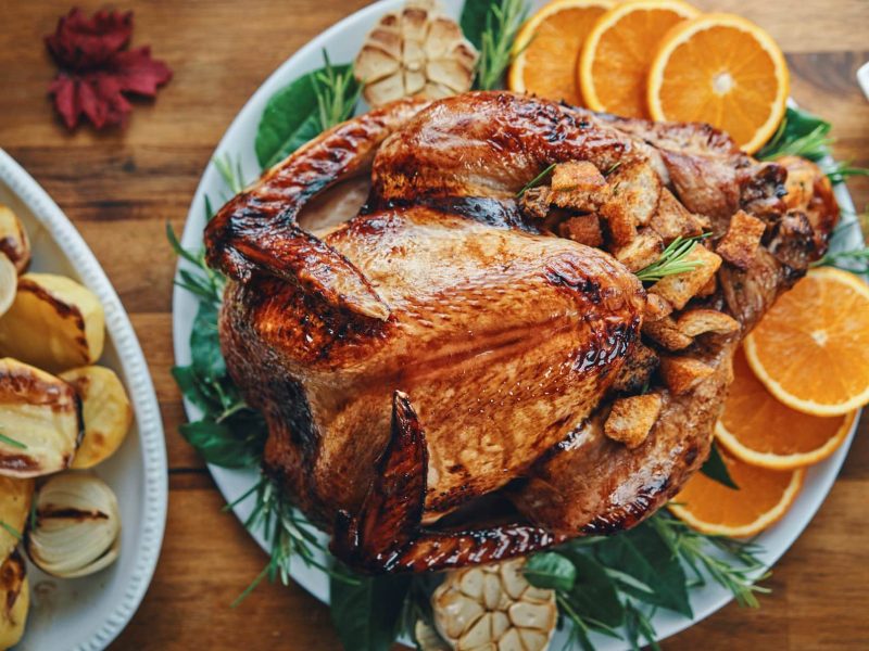 In der Draufsicht sieht man einen Thanksgiving-Truthahn auf einem Teller, dekoriert mit Orangenscheiben und Kräutern. Drumherum sieht man einige Beilagen.