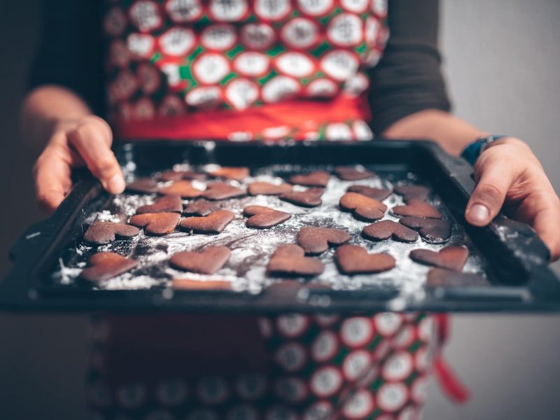 Frau mit Retro-Schürze hält Blech mit verbrannten Keksen.