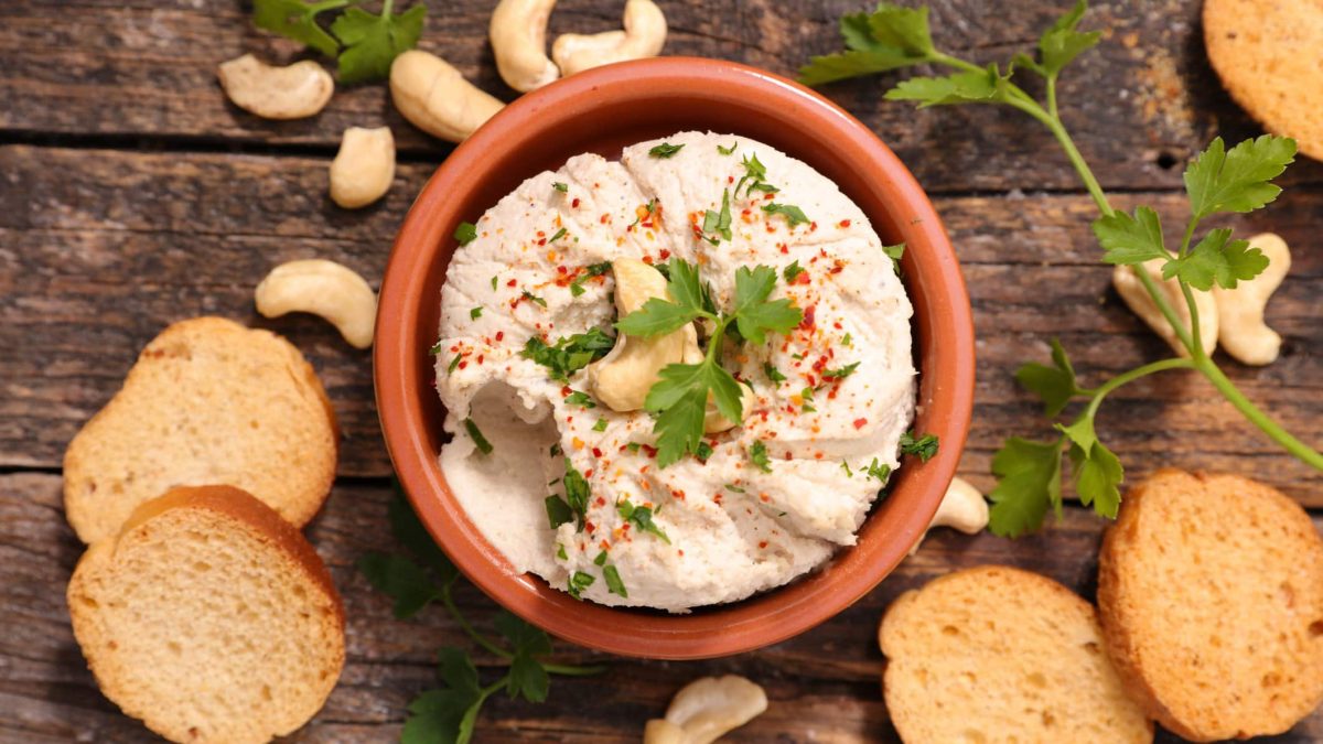 Eine Schale vegane Auberginencreme in der Draufsicht, drumherum liegen Zwiebackscheiben und Cashews.