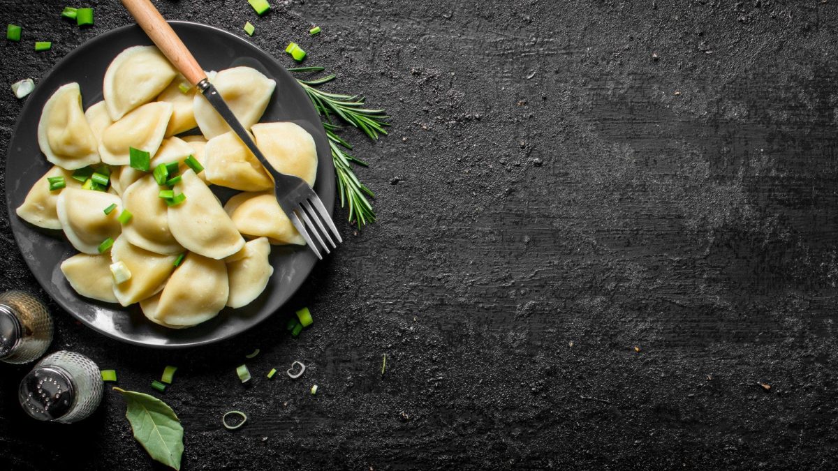 Ein Teller mit veganen Kasnudeln auf dunklem Untergrund in der Draufsicht. Darüber ist etwas Schnittlauch gestreut, außerdem stehen Salz und Pfeffer neben dem Teller.
