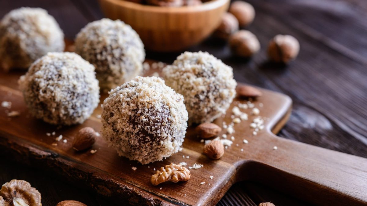 Auf einem Brettchen liegen fünf vegane Mandel-Kokos-Kugeln.