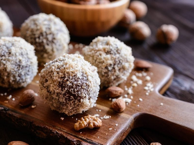 Auf einem Brettchen liegen fünf vegane Mandel-Kokos-Kugeln.