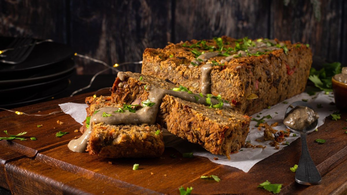 Auf einem Brett liegt ein angeschnittener veganer Nussbraten, bestreut mit Petersilie. Im Hintergrund ist eine Lichterkette erkennbar.
