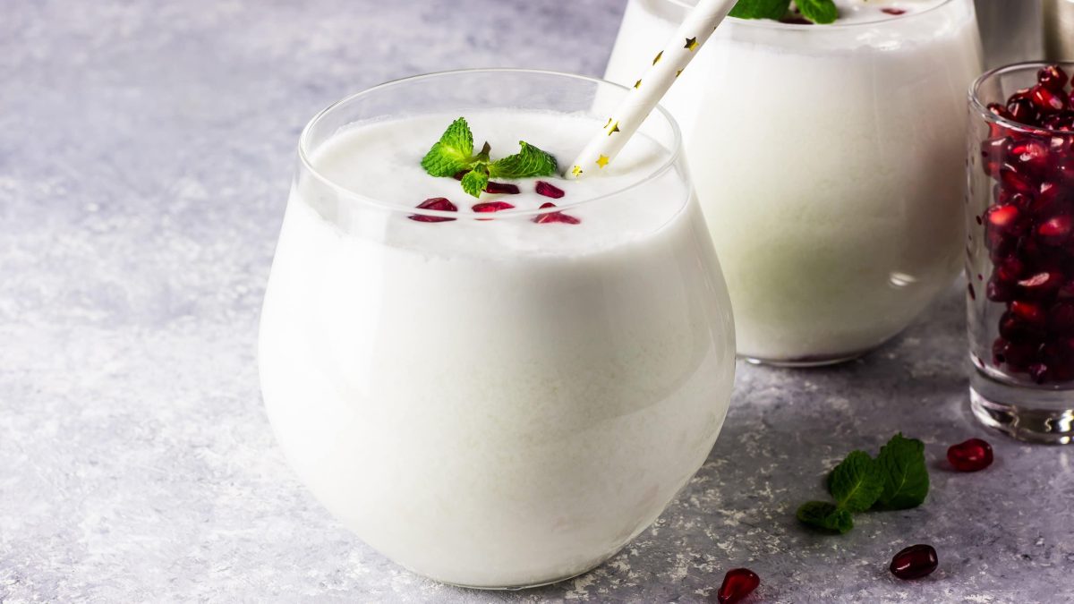 Zwei Gläser White Christmas Mojito dekoriert mit Granatapfelkernen und MInzblättern. Daneben steht ein Glas mit Granatapfelkernen.