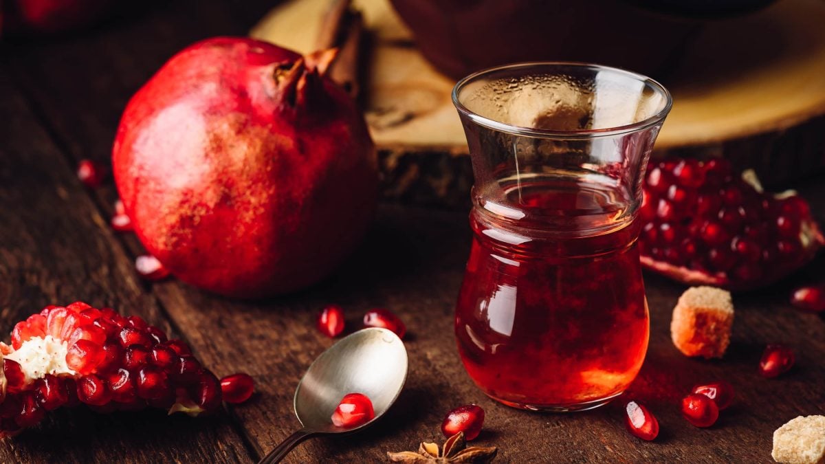 Euf einem Tisch steht ein Glas mit Granatapfeltee. Daneben liegt ein Granatapfel.