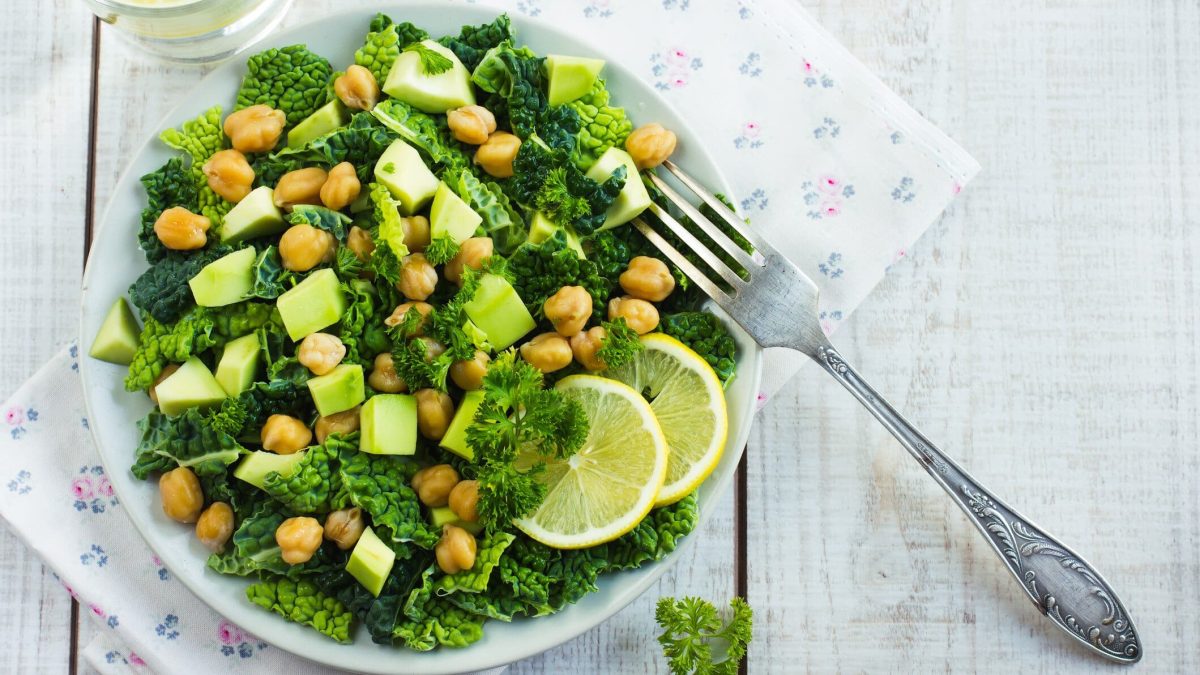 Ein Teller Wirsingsalat mit Kichererbsen und Avocado auf weißem Holz in der Draufsicht mit einer silbernen Gabel.