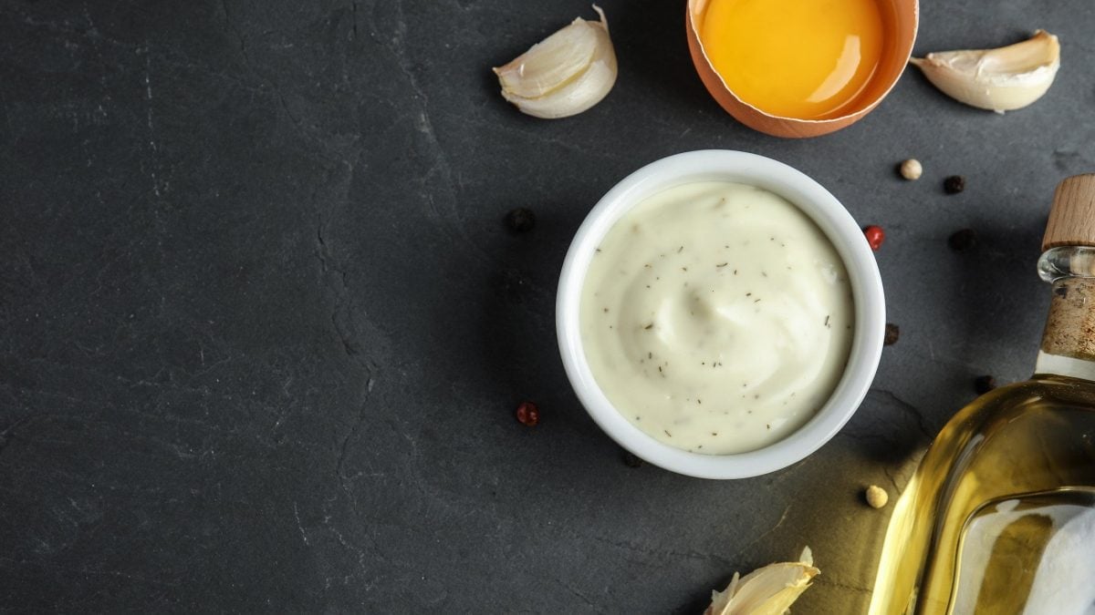 Schale mit Aioli auf dunklem Untergrund umgeben von Zutaten