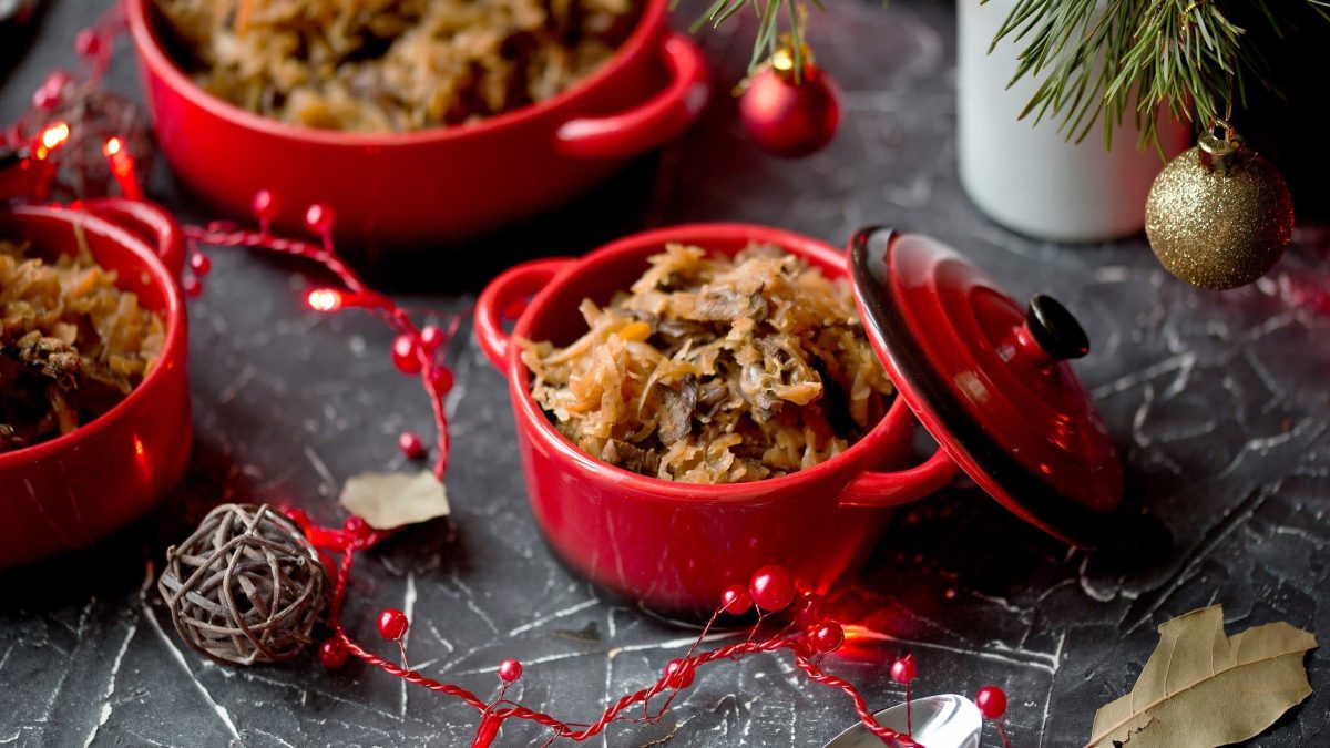 Topf mit Bigos umgeben von weihnachtlicher Dekoration auf dunklem Untergrund.