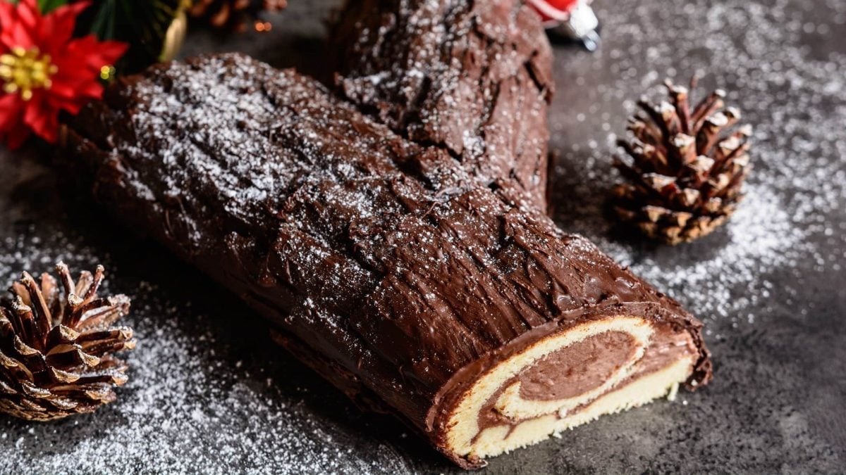 Bûche de Noël in weihnachtlichem Ambiente auf dunklem Untergrund.