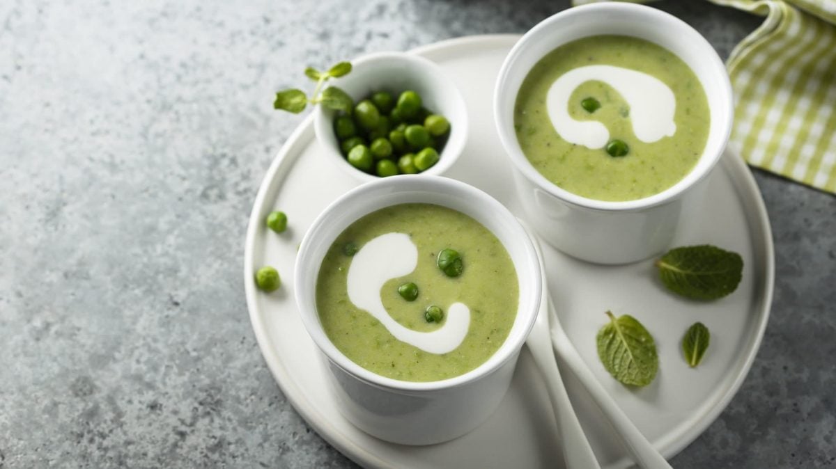 Unsere feine Erbsensuppe angerichtet in zwei Becherschalen, die auf einem weißen Teller Platz finden.