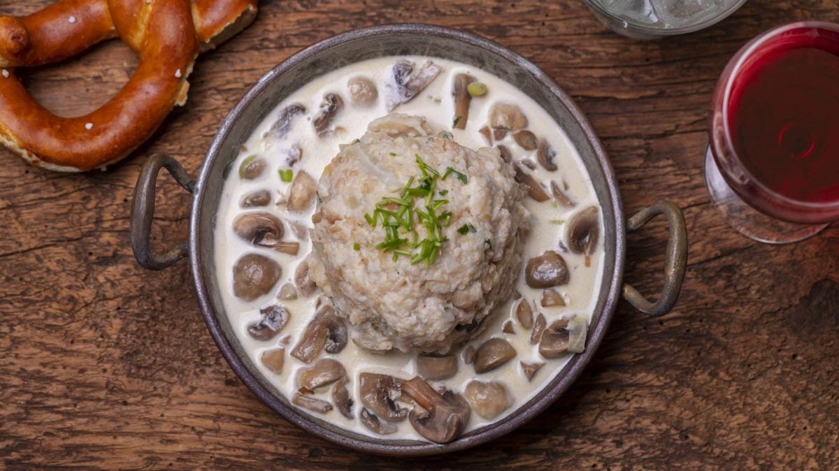 Unser Brezenknödel wird in einer Pilz-Rahm-Soße in einer Schüssel und mit einem Glas Rotwein angerichtet.