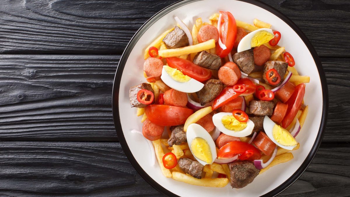 Pique Macho: Bolivianisches Gericht auf einem Teller mit Tomaten, Rindfleischstücken, Chorizo, Pommes, gekochtem Ei, Tomaten, Chili und Soße