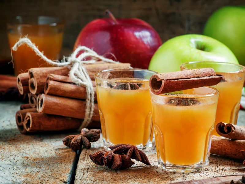 Drei Gläser mit Apfel-Glüh-Gin umgeben von den Zutaten