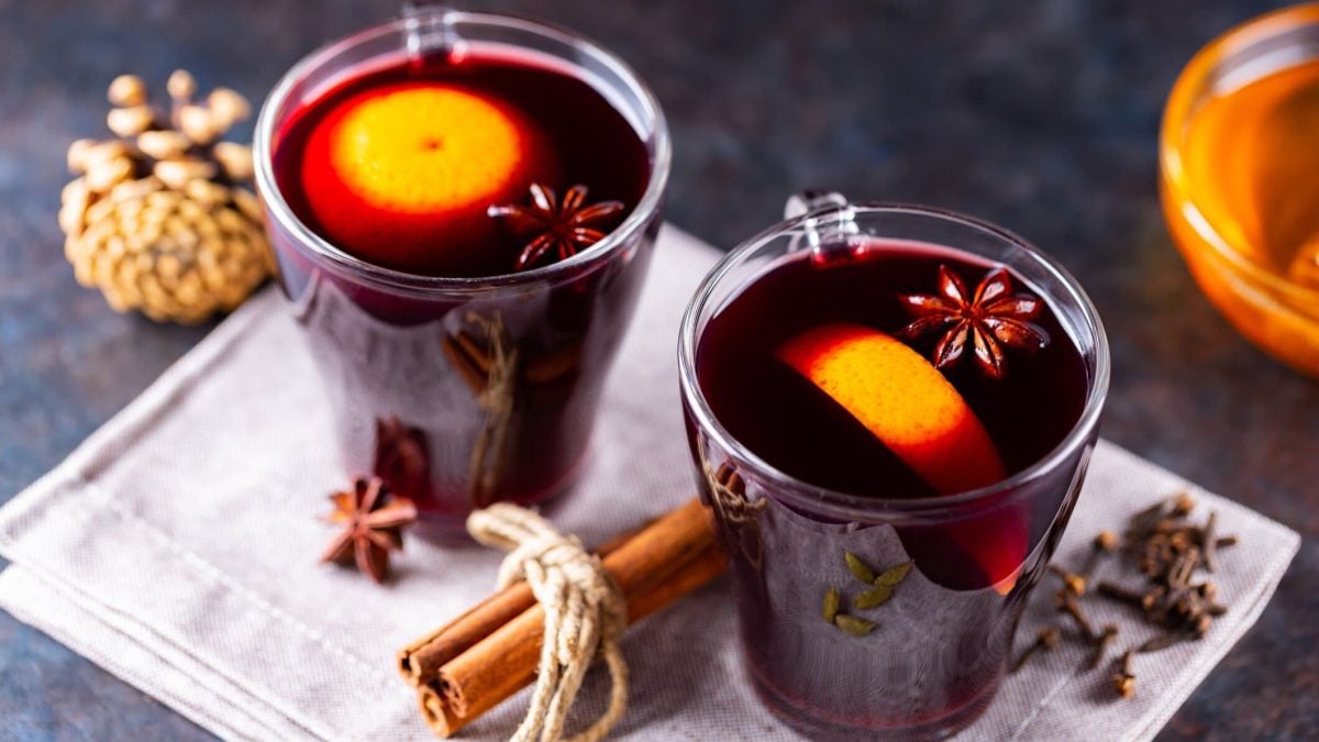 Zwei Tassen Glühwein mit Orangen und Gewürzen auf dunklem Untergrund