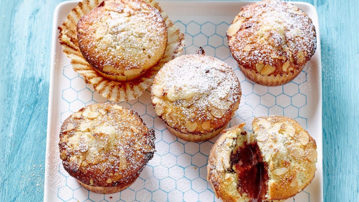 Auf einem weißen Keramikteller liegen 5 Mandel-Muffins mit Espresso-Füllung. Ein Muffin ist angeschnitten, man erkennt im Inneren die Espressofüllung.