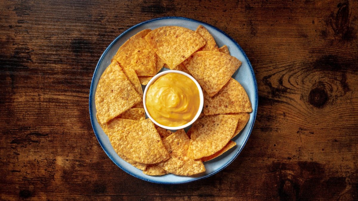 Teller Nachos mit Käsesoße auf hölzernem Untergrund