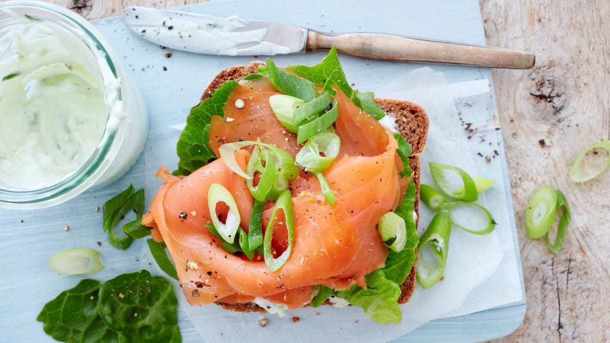 Vollkorn-Sandwich mit Lachs auf Holzbrett.