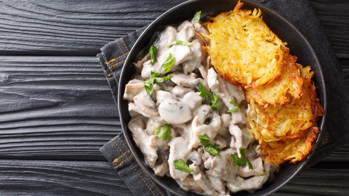 Zürcher Geschnetzeltes mit Rösti auf schwarzem Teller.