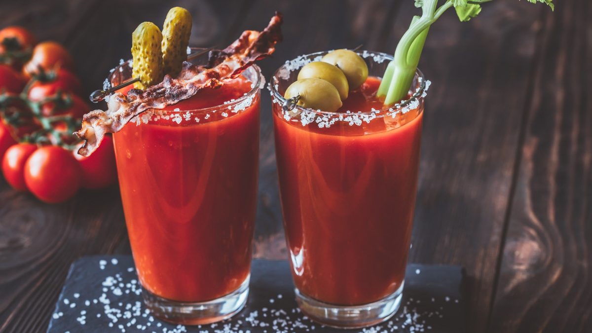 Bloody Mary: Longdrink mit Tomate, Wodka, Tabasco und Worcestersauce garniert mit Bacen, Oliven, Sellerie und saurer Gurke auf einem Holzbrett