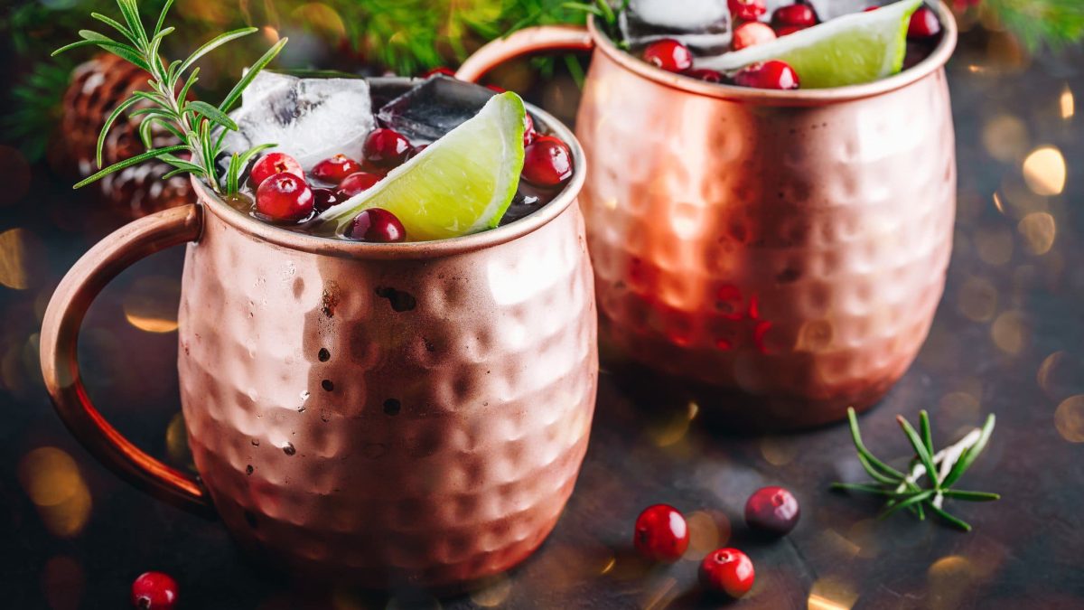 Zwei Kupferbecher mit Cranberry Moscow Mule, Eiswürfeln, Rosmarin und einer Limettenspalte.