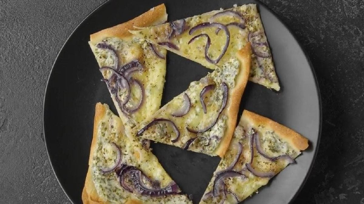 Unser Flammkuchen mit Mozzarella liegt in Dreiecke geschnitten auf einem schwarzen Teller.