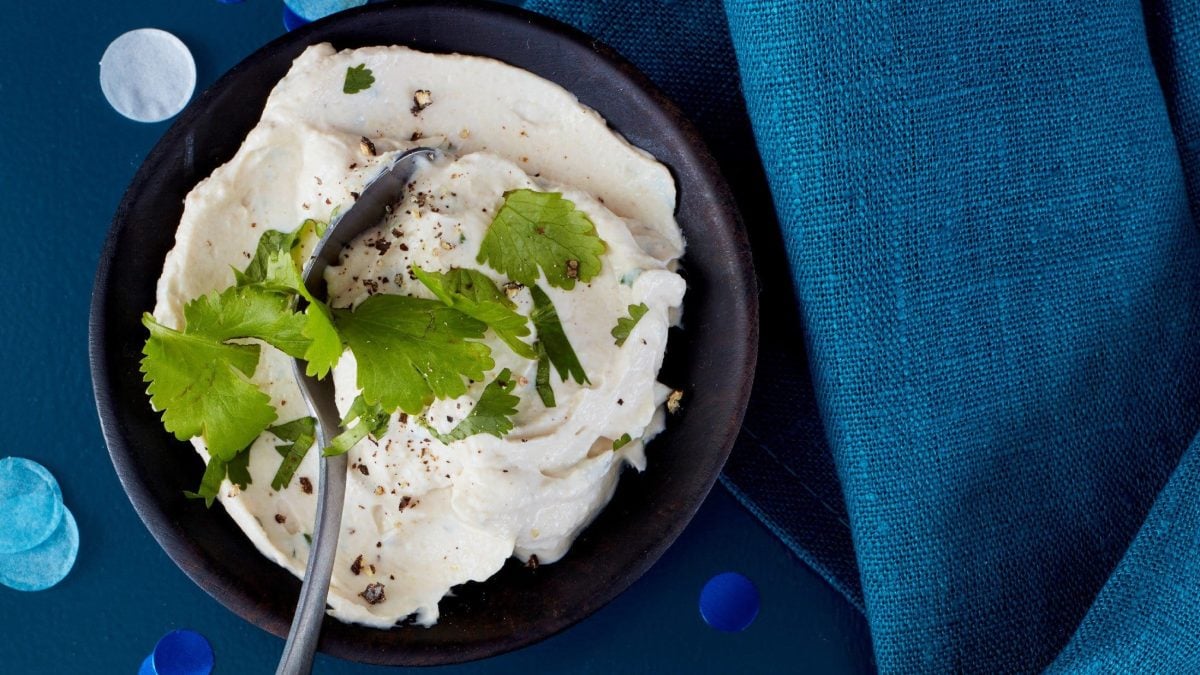 Frischkäse Dip mit Sesamcreme garniert mit frischem Koreander in einer schwarzen Schale auf blauem Tuch serviert