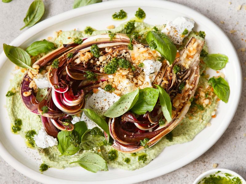 Ein Teller gebackener Radicchio mit Erbsen-Basilikum-Hummus und zerbröseltem Feta in der Draufsicht.