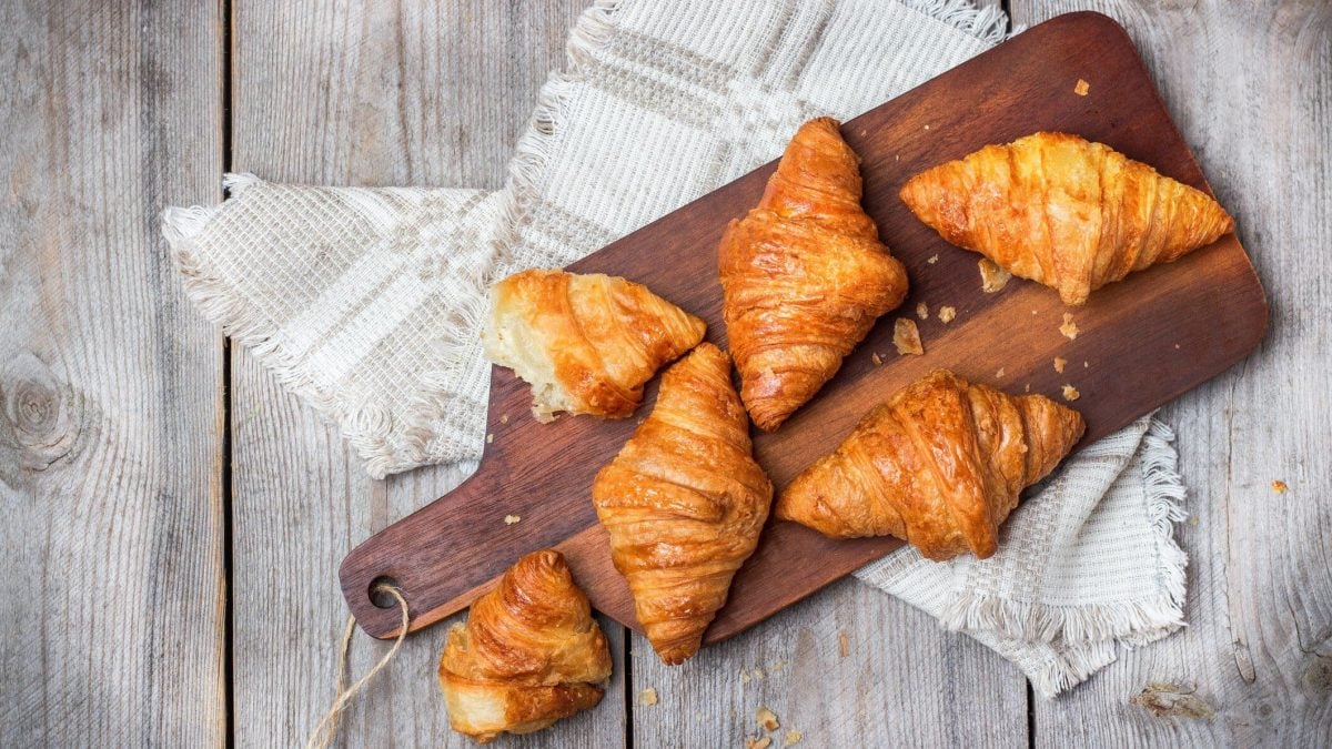 In der Draufsicht sieht man Kartoffelcroissants auf einem Holzbrett liegen, das Brett liegt auf weißem Holz.
