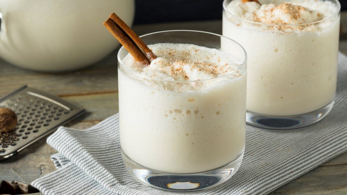 Zwei Gläser mit heißer Milch und Whiskey, dekoriert mit Zimtstangen.