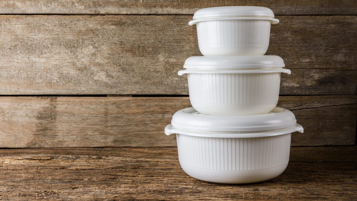 Vor einem Hintergrund au Holz stehen drei weiße Tupperware Boxen mit einem Deckel. Diese sind der Größe nach gestapelt.