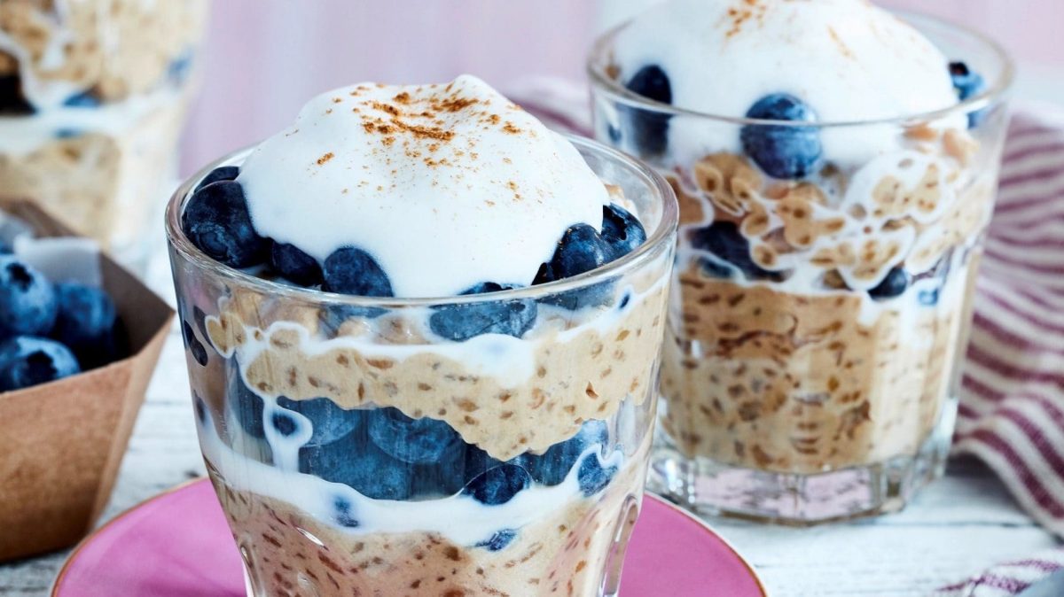Auf einem Tisch stehen drei Gläser. In ihnen ist geschichteter Kaffee-Milchreis mit Heidelbeeren.