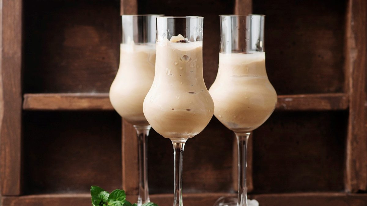 Schoko-Likör mit Kaffee in drei Gläsern vor einem hälzernen Hintergrund. Der Likör ist angerichtet mit Kaffeebohnen.
