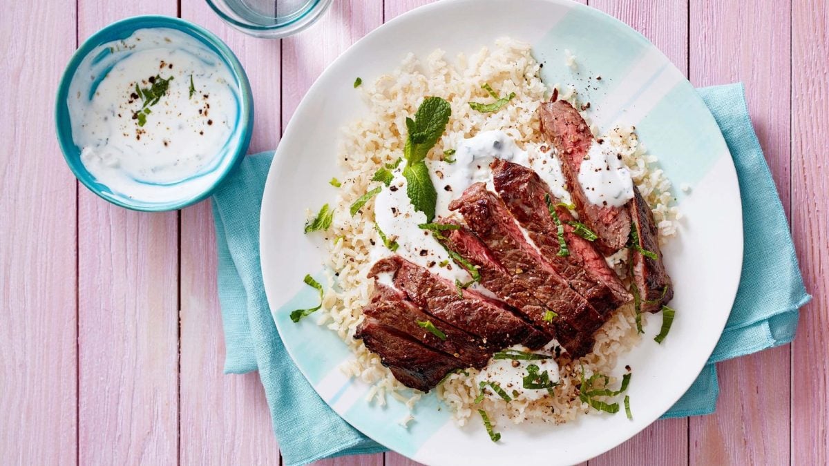 Steak in streifen geschnitten mit Joghurt-Minzsoße auf Reis, auf einem weißen Teller mit blauen Servietten serviert