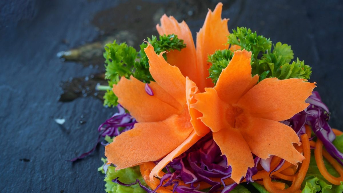 Eine Möhre wurde tourniert. Also on Form einer Blüte geschnitten. Sie dekoriert ein Salatblatt.