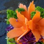 Eine Möhre wurde tourniert. Also on Form einer Blüte geschnitten. Sie dekoriert ein Salatblatt.