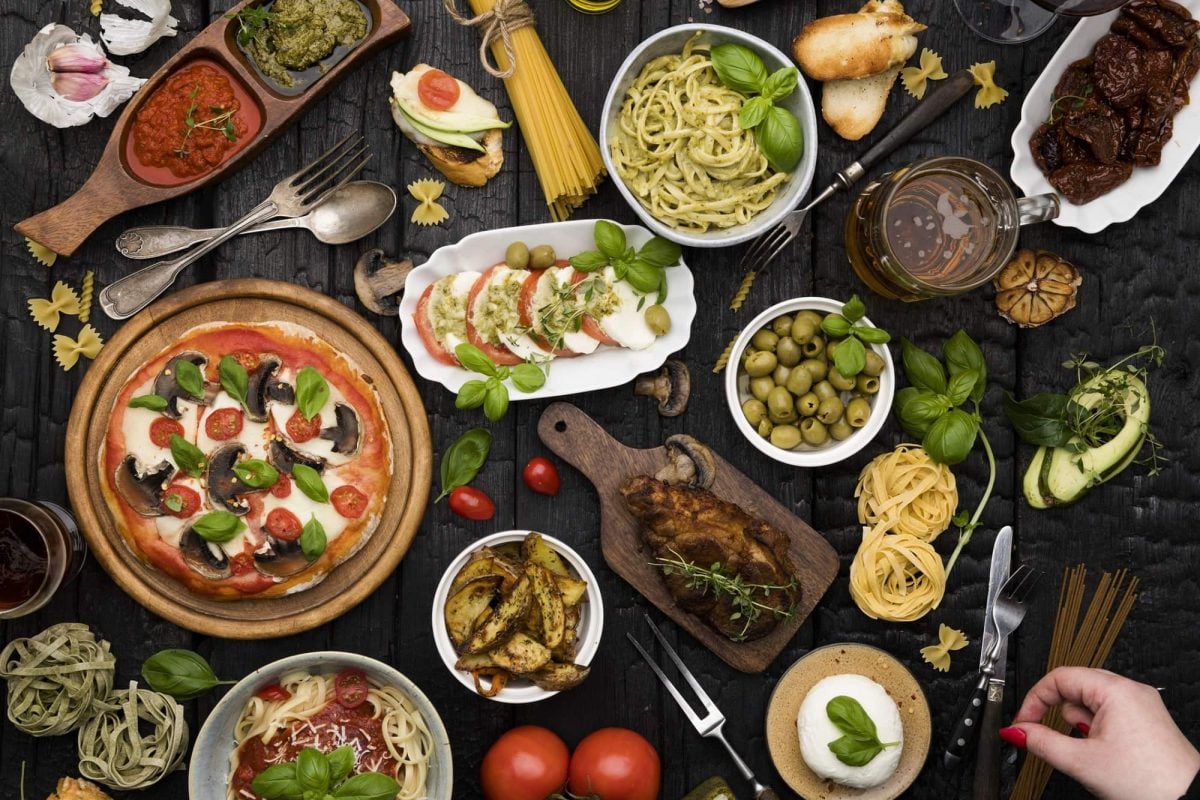 Verschiedene Gerichte, Beilagen und Gewürze stehen nebeneinander auf einem dunklen Tisch. Die Gerichte sind zum Tag des Buffets angerichtet