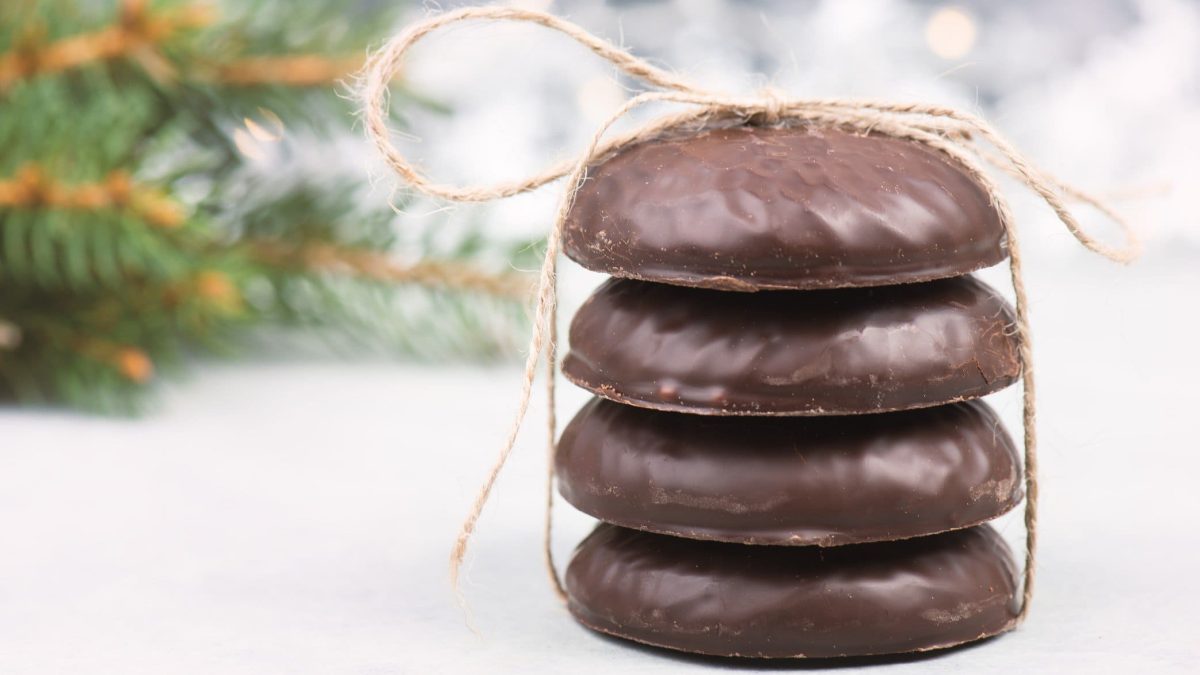 Ein Stapel vegane Elisenlebkuchen mit Band zusammengebunden vor einem hellen, unscharfen Hintergrund mit Tannenzweigen.