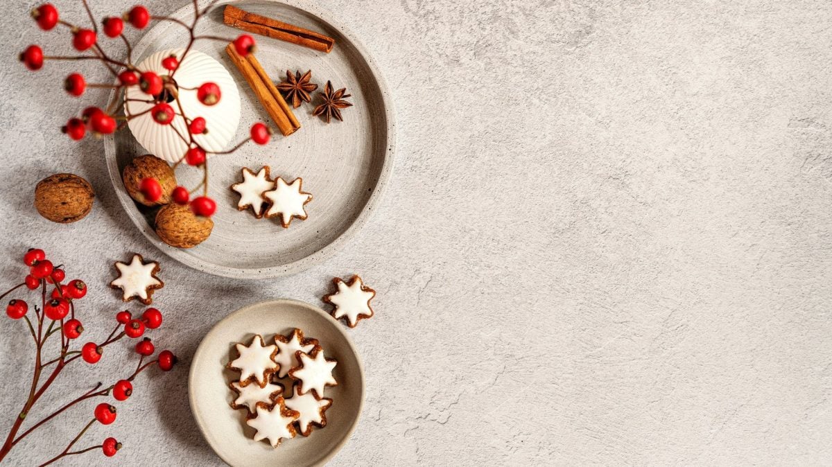 Ein Teller und eine Schale mit veganen Zimtsternen in der Draufsicht auf hellem Untergrund, außerdem Walnüsse, Anis und Zimtstangen sowie ein Weihnachtsstrauß.