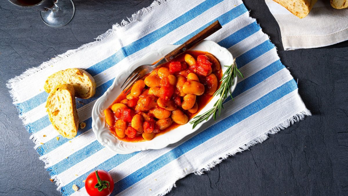 Weißer Teller mit griechischen Bohnen in Tomatensauce. Es handelt sich um Gigantes Plaki.