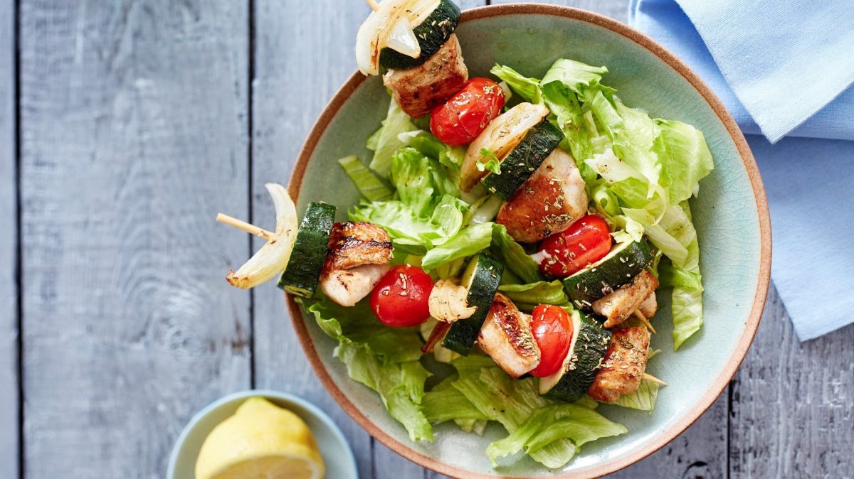 In einer Schüssel liegen zwei saftige Puten-Zucchini-Spieße auf Salatblättern.