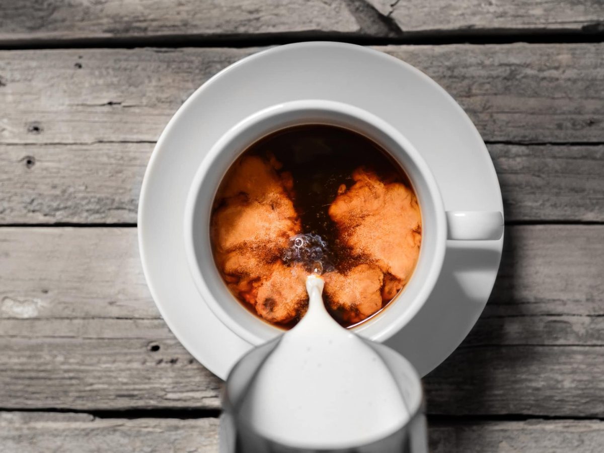 Milch wird in eine Tasse Kaffee gegossen.